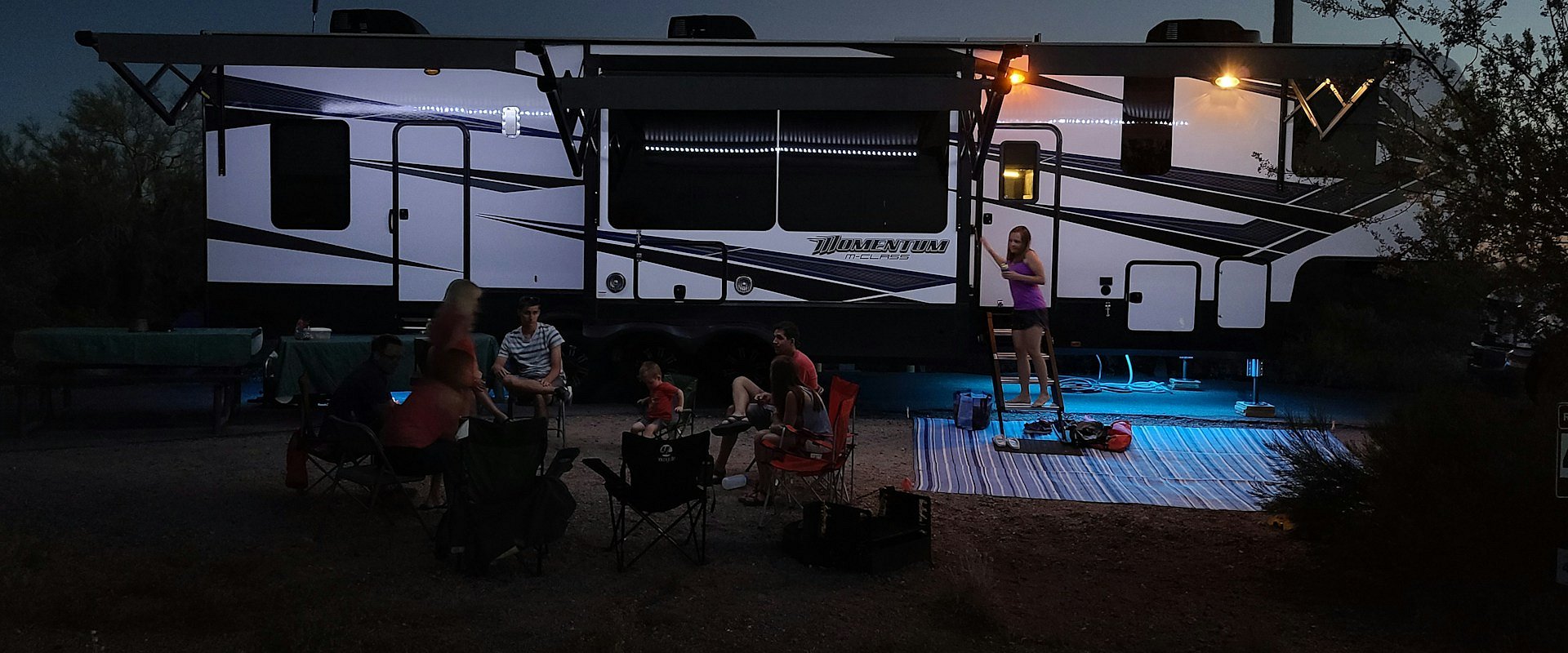 A travel trailer at a campsite beneath tall trees
